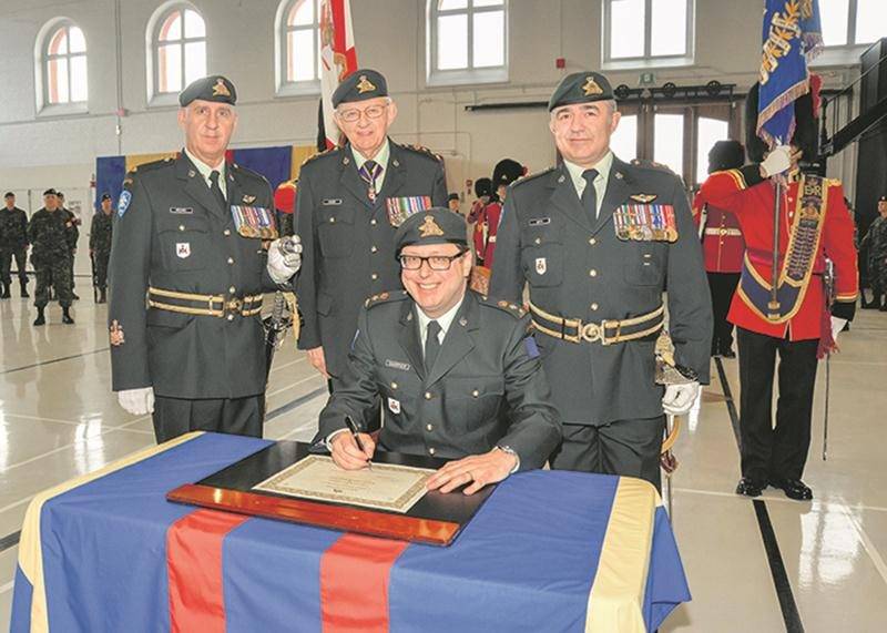 Benoit Chartier signe le parchemin officialisant son titre de lieutenant-colonel honoraire du 6e Bataillon Royal 22e Régiment. Derrière M. Chartier, de gauche à droite, l’adjudant-chef Robyn Bédard (sergent-major régimentaire du 6e Bataillon Royal 22e Régiment), le lieutenant-général à la retraite Richard J. Evraire (colonel du Royal 22e Régiment) et le lieutenant-colonel Steve Hétu (commandant du 6e Bataillon Royal 22e Régiment).
