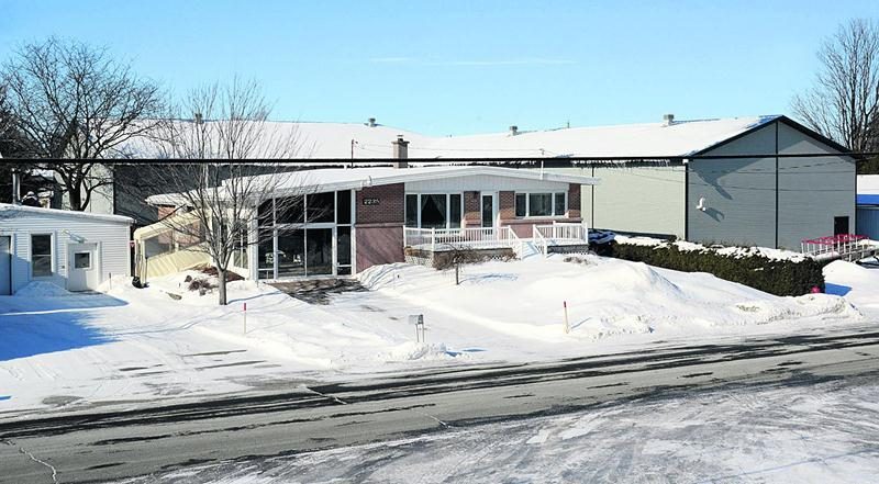 Le bungalow de Noëlla Paquette, rue Demers à Sainte-Marie-Madeleine, paraît écrasé par les murs du garage en « L » qui bordent maintenant son terrain sur deux côtés. Il chevauche un terrain résidentiel et une parcelle devenue commerciale (à l’arrière) à la suite d’une procédure douteuse de changement de zonage. Photo François Larivière | Le Courrier ©