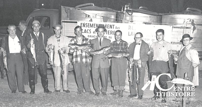 Léo-Paul Robert, président du Club Maska, est sixième en partant de la gauche. À l’arrière, le camion-citerne ayant servi au transport des poissons dans la nuit du 23 au 24 avril 1957.   Centre d’histoire de Saint-Hyacinthe, CH116.