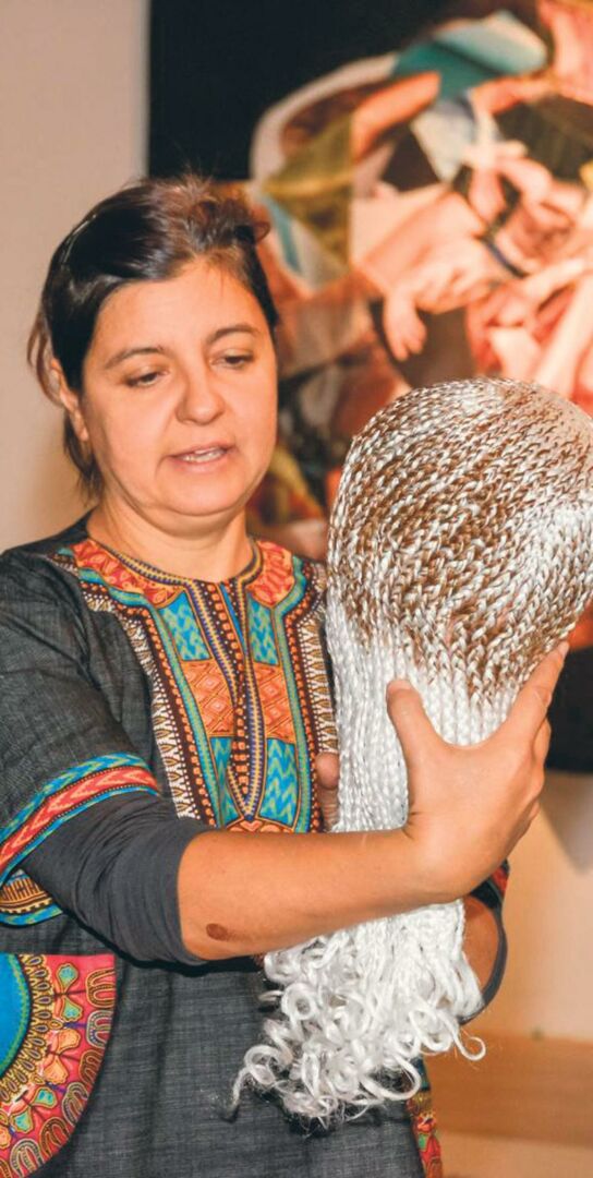 L’artiste Giorgia Volpe tenant l’une des « têtes d’Aissatou », une œuvre consistant en des têtes de coiffure en plastique recouvertes de tresses de cheveux synthétiques. Photo François Larivière | Le Courrier ©