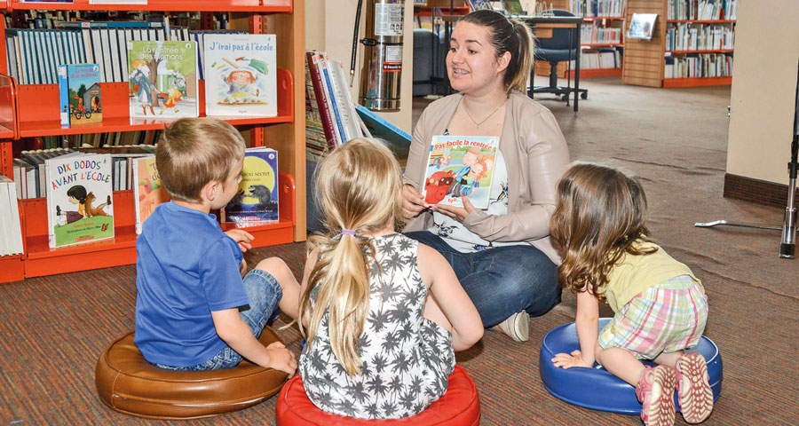 Andréanne Morin, de la Maison de la famille des Maskoutains, présente à trois futurs élèves l’un des livres de la nouvelle section « Prêt pour la maternelle ». Photo François Larivière | Le Courrier ©