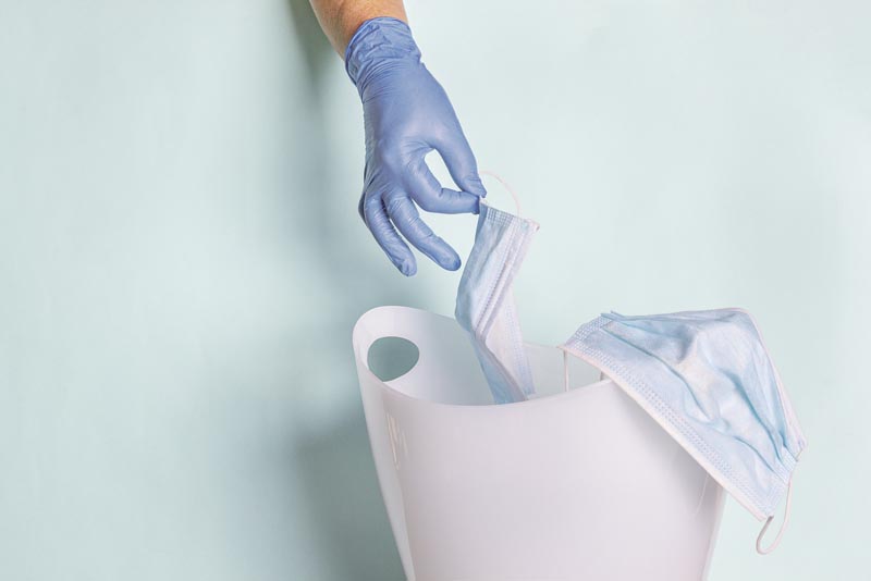 Female hand in disposable rubber gloves throws face mask into trash can. Coronavirus outbreak, quarantine concept. Protect covid-19 during global pandemic