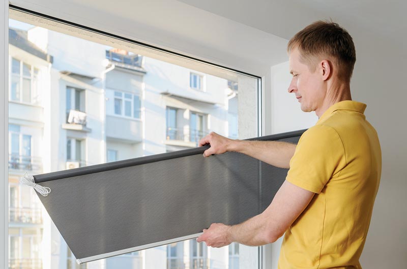 Man is holding fabric window blind gray.