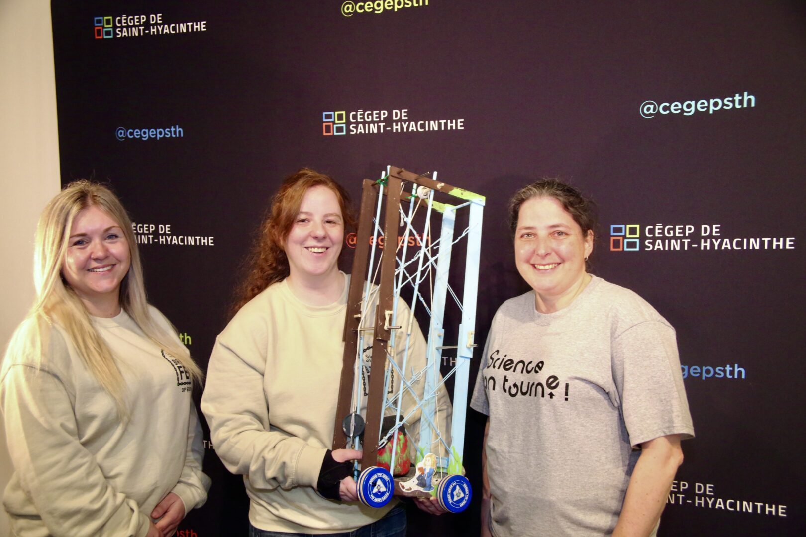 Judy Drolet-Bolduc, conseillère responsable du concours pour le Centre de démonstration en sciences physiques du Cégep Garneau, institution qui chapeautait l’événement, la représentante du Cégep de Saint-Hyacinthe, Stacy Filion, avec son engin et Anne Lemieux, technicienne en loisirs au Cégep, qui coordonnait l’accueil de la finale nationale de Science, on tourne!. Photo Robert Gosselin | Le Courrier ©